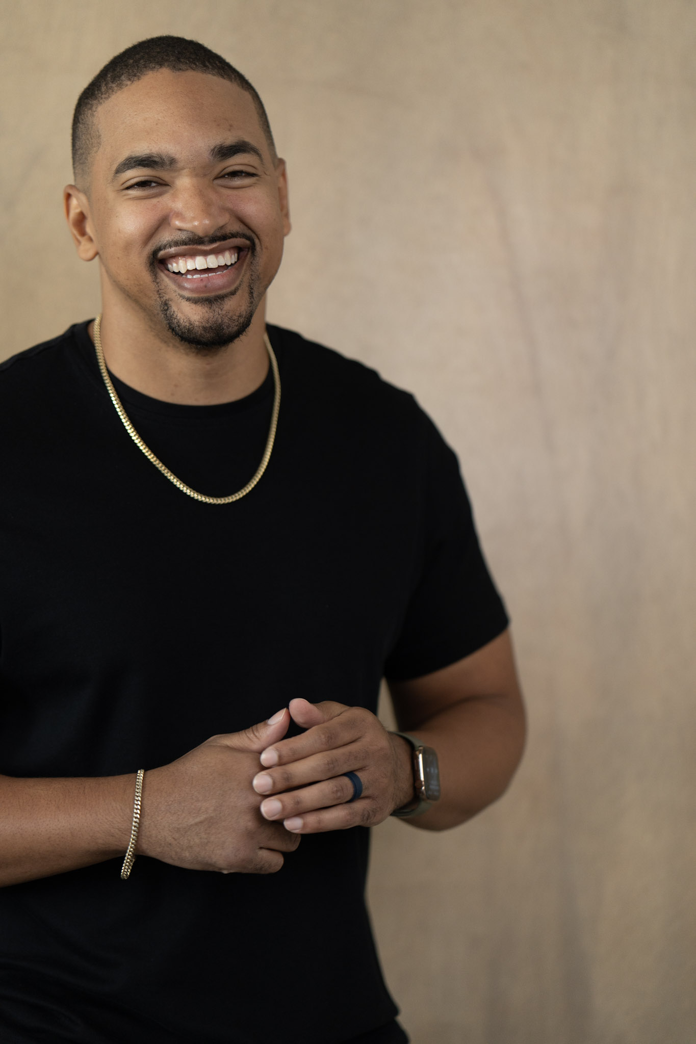 Jared Langley smiling in a black tee with gold chain, hands clasped
