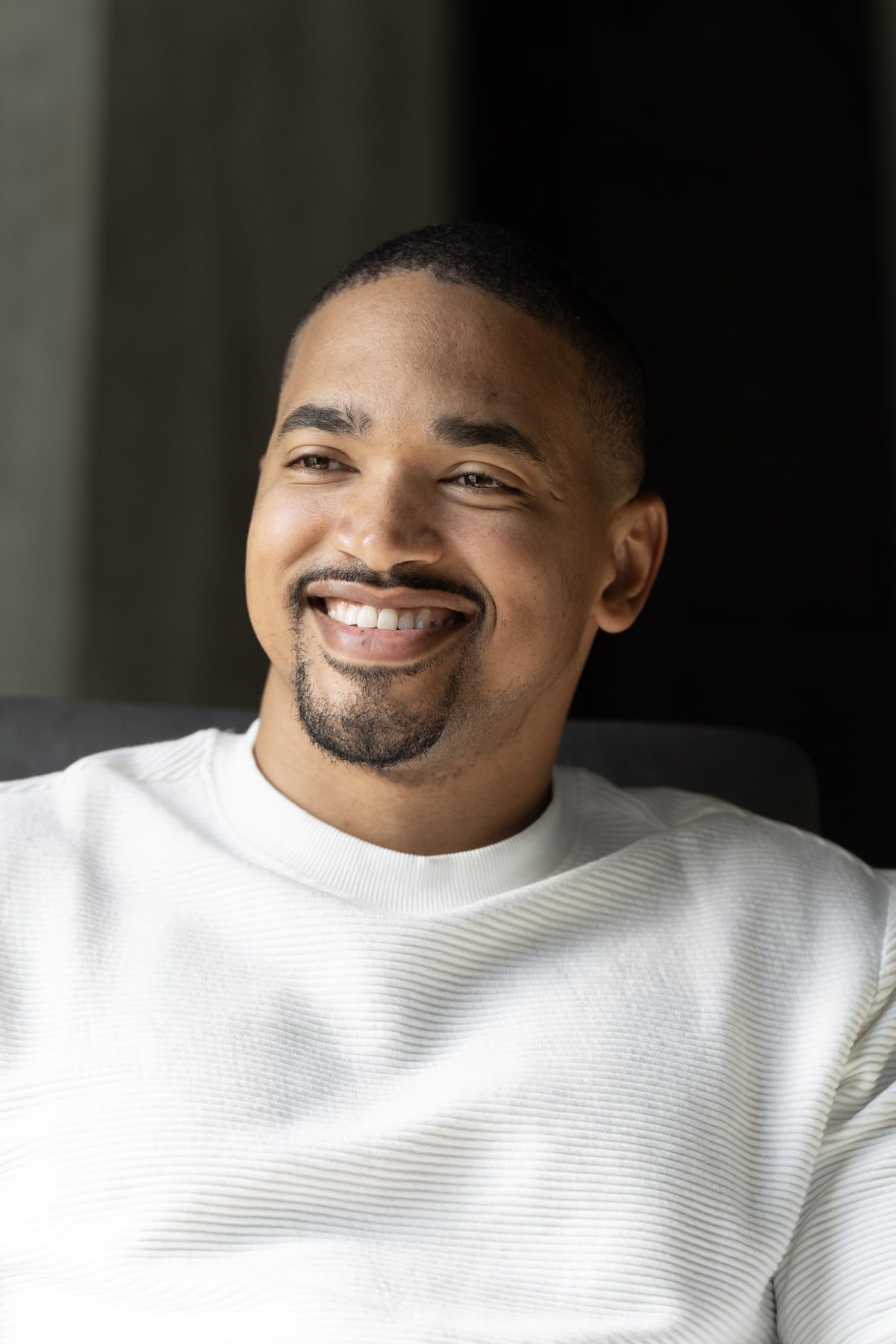Jared Langley seated in a white ribbed sweater, smiling off camera, studio portrait by Clifton Albright