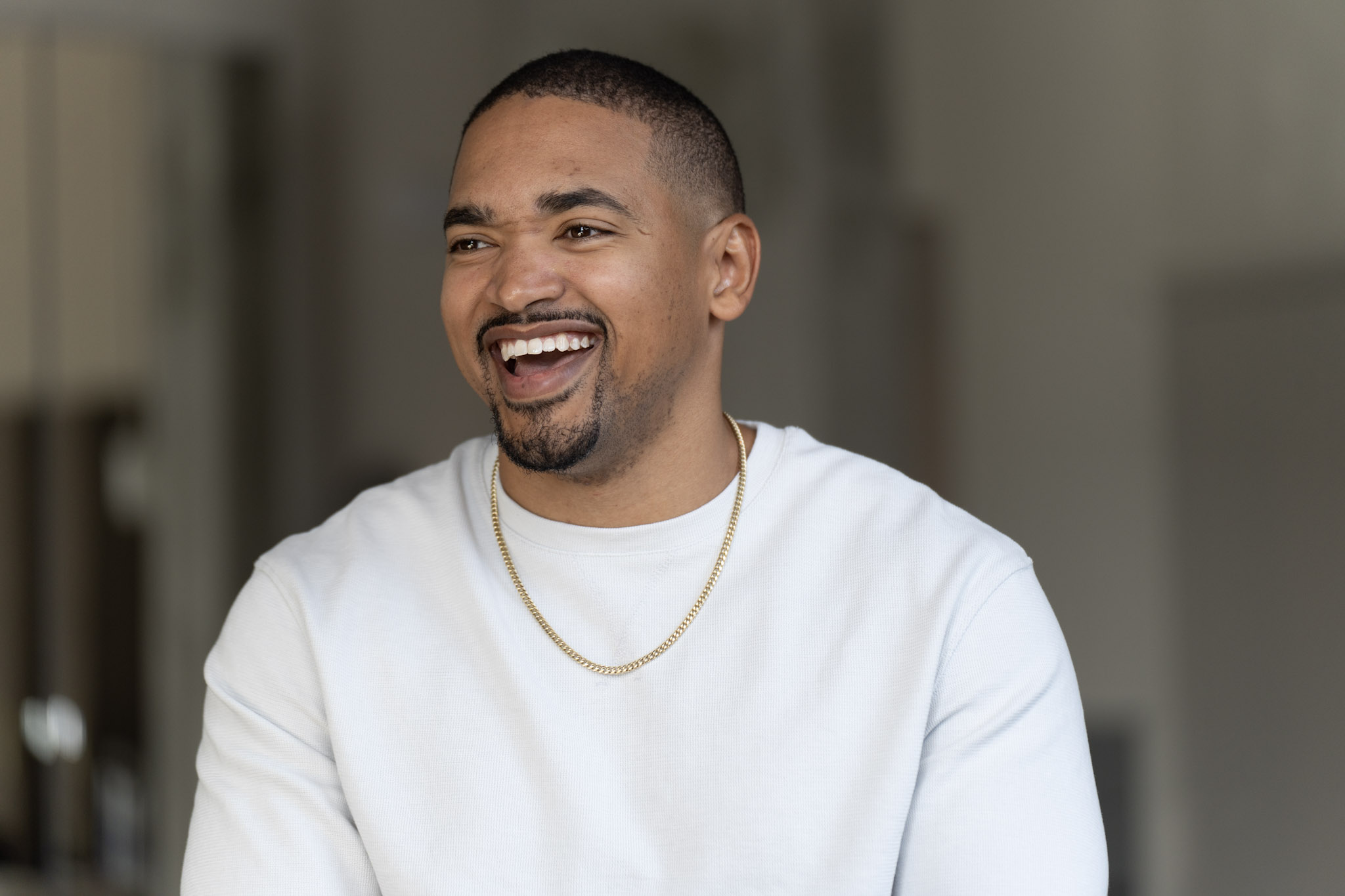 Jared Langley laughing, wearing a white sweater with a gold chain