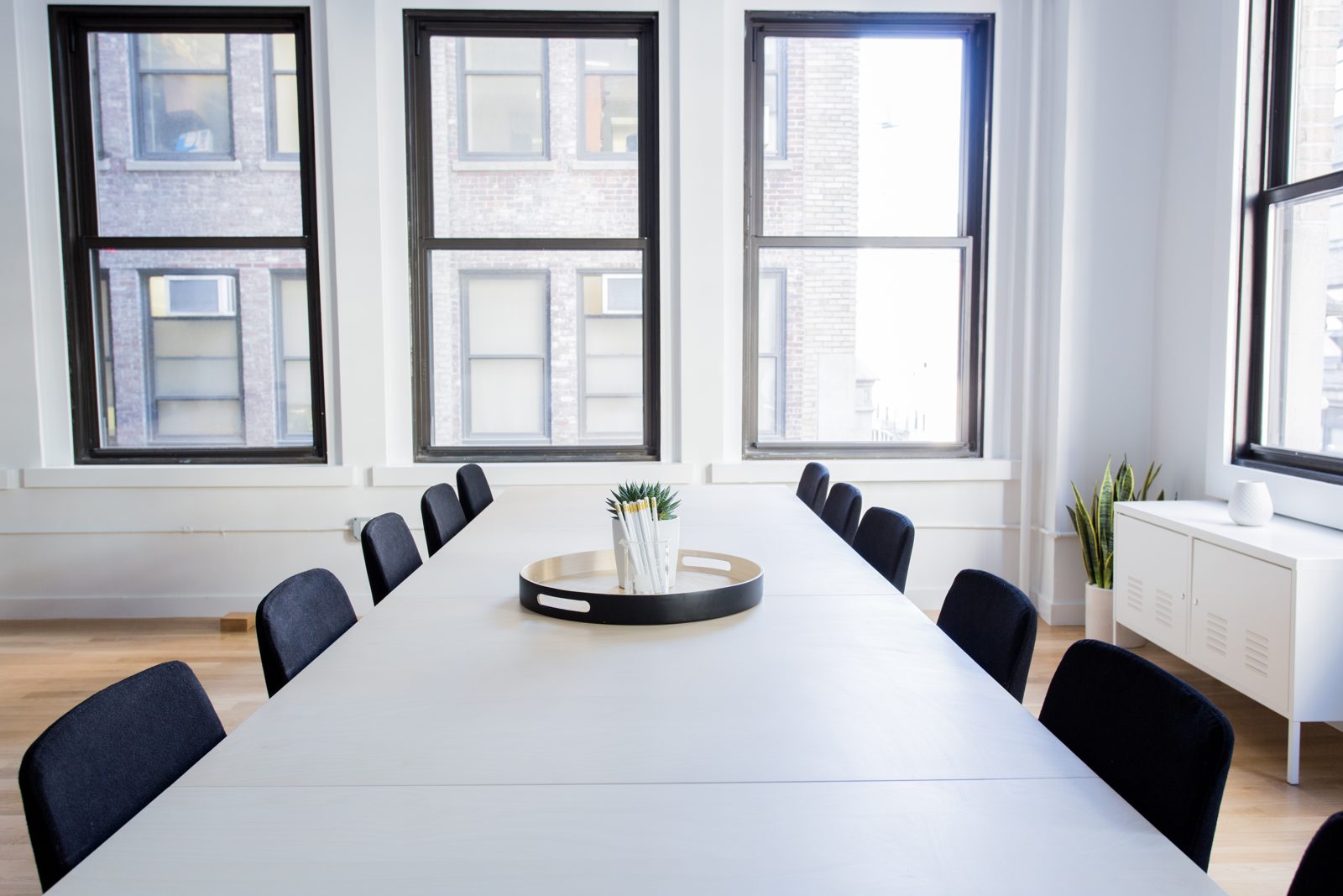 An empty meeting room, long white table and dark chairs, windows on two sides