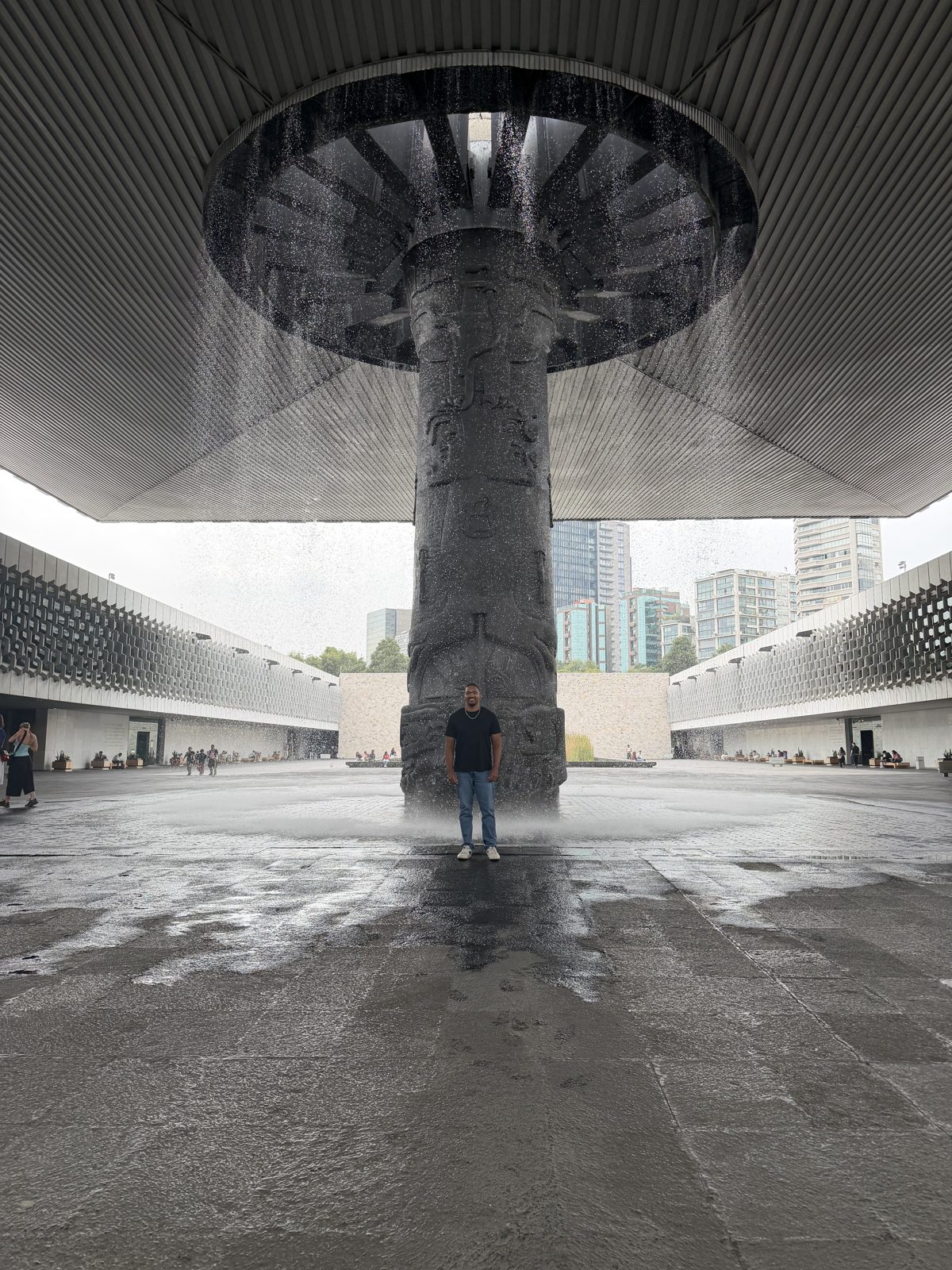 Jared standing small beneath a towering carved column and a curtain of falling water